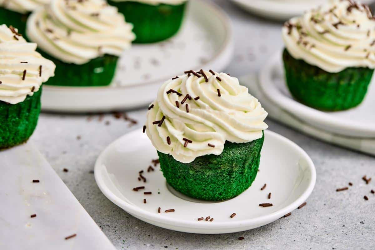 A St. Patrick&rsquo;s Day Green Matcha Cupcakes sits on a small white plate, with more cupcakes visible in the background.
