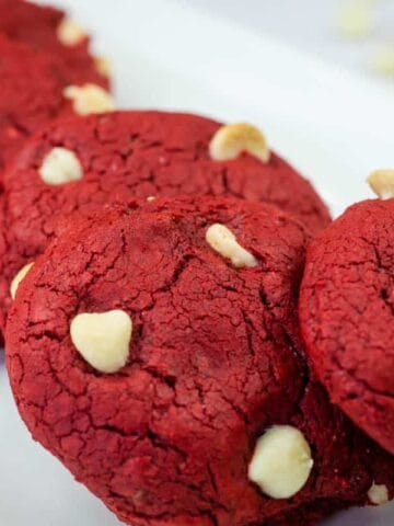 Four red velvet cookies with white chocolate chips arranged on a white plate.