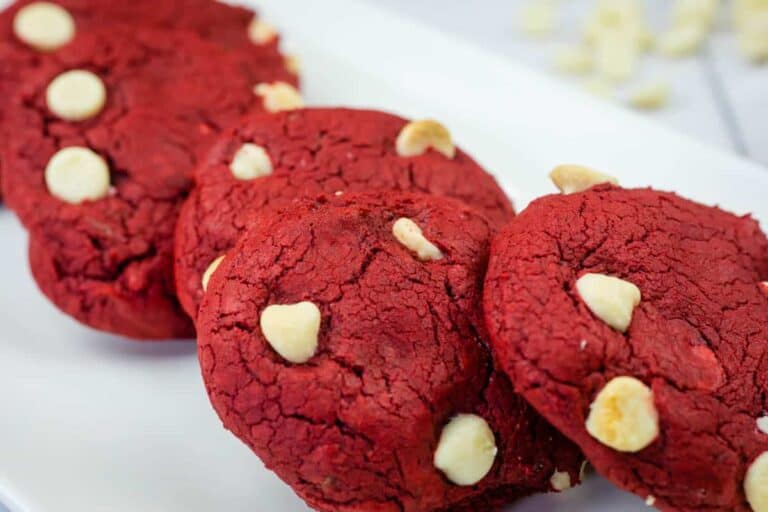 Four red velvet cookies with white chocolate chips arranged on a white plate.