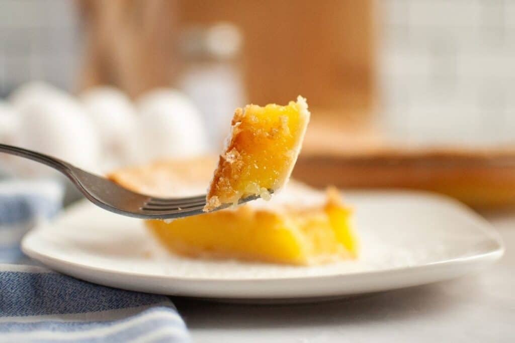 A close-up of a fork holding a bite of vinegar pie above a white plate.