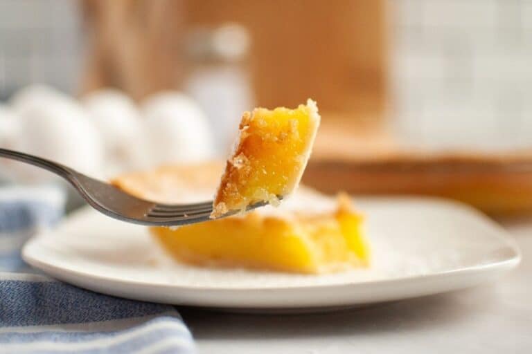 A close-up of a fork holding a bite of vinegar pie above a white plate.