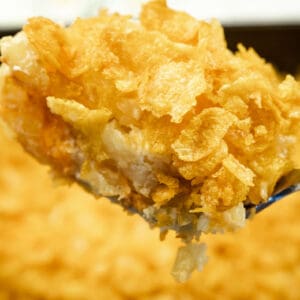 A close-up of a spoonful of casserole topped with crispy corn flakes, with the rest of the casserole in the background.
