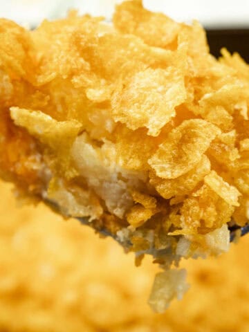 A close-up of a spoonful of casserole topped with crispy corn flakes, with the rest of the casserole in the background.