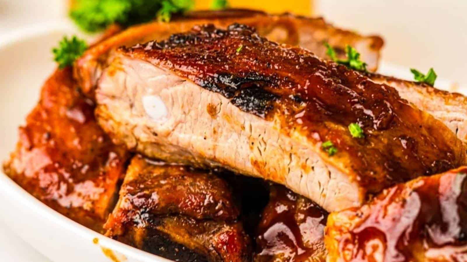 Close-up of Grilled ribs covered in sauce, garnished with chopped parsley, served on a white plate.