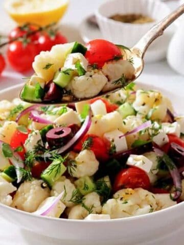 A spoon holds a serving of Greek Cauliflower Salad above the bowl.