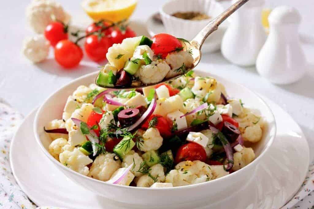 A spoon holds a serving of Greek Cauliflower Salad above the bowl.