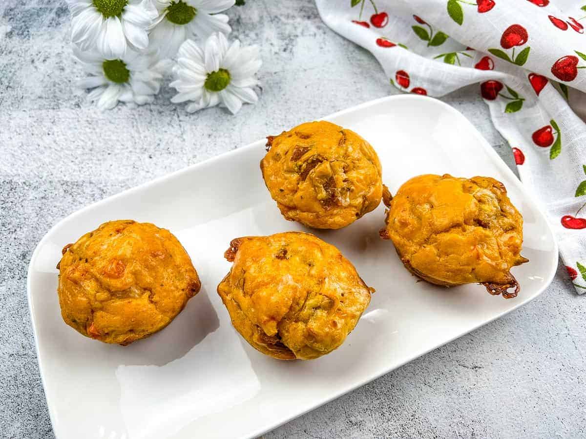 Four pizza muffins on a white plate with flowers.