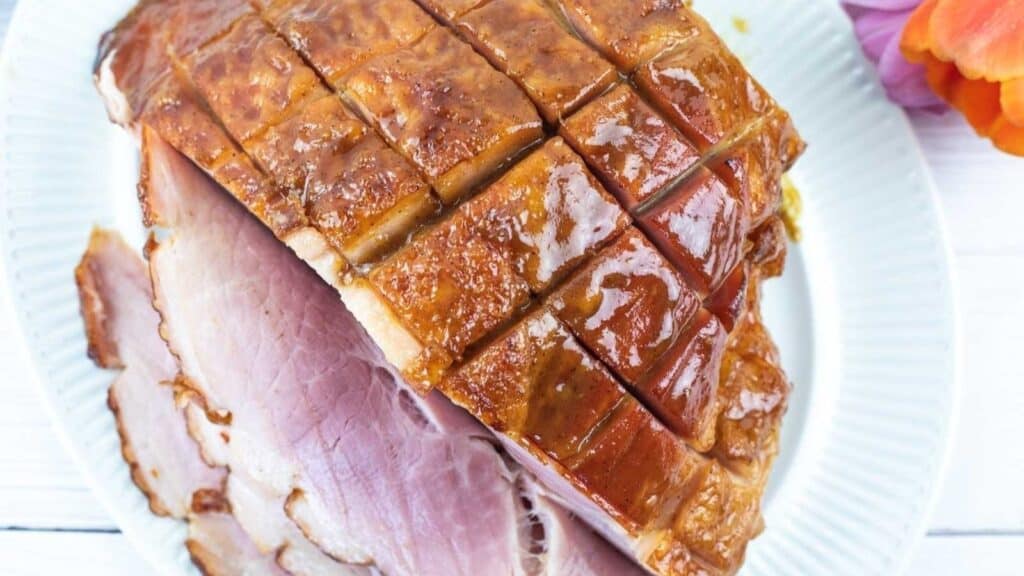 Sliced glazed ham with a crisscross pattern on top, served on a white plate.