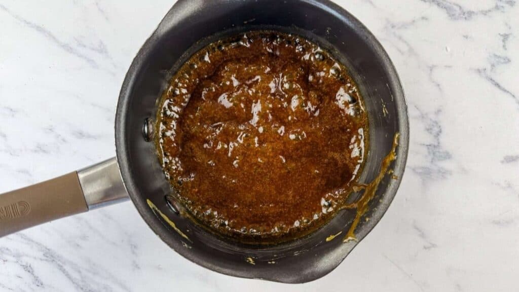 A small saucepan filled with a bubbling brown sugar mixture on a white marble countertop.