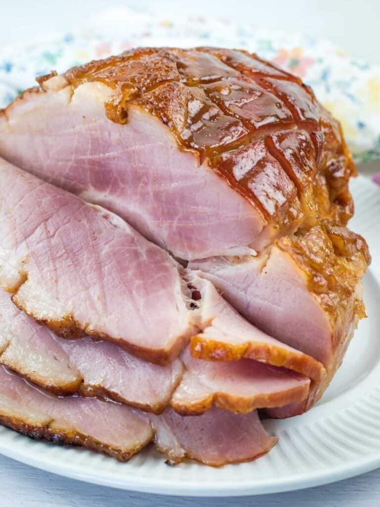 Sliced glazed ham arranged on a white plate, displaying a caramelized outer layer and juicy pink interior.