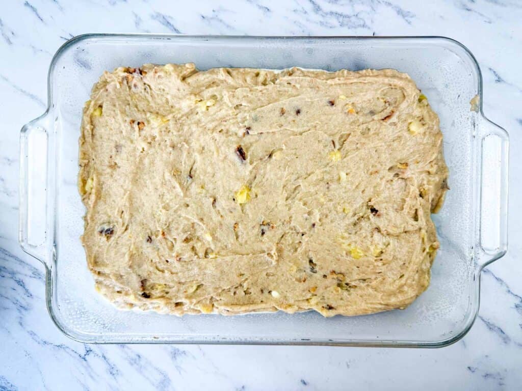 A glass baking dish filled with an even layer of unbaked banana bread batter on a marble countertop.