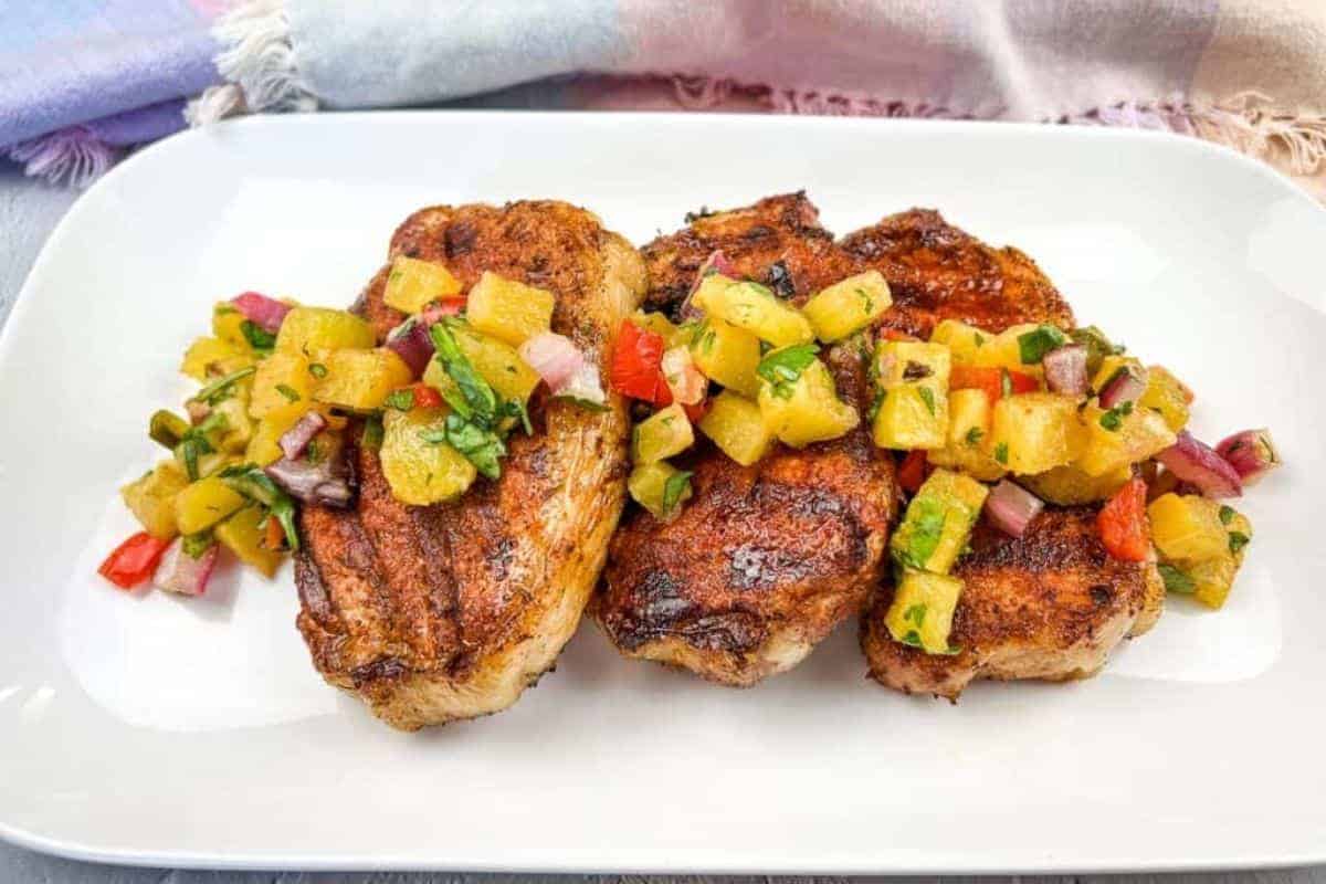 Grilled pork chops with pineapple salsa on a white plate.