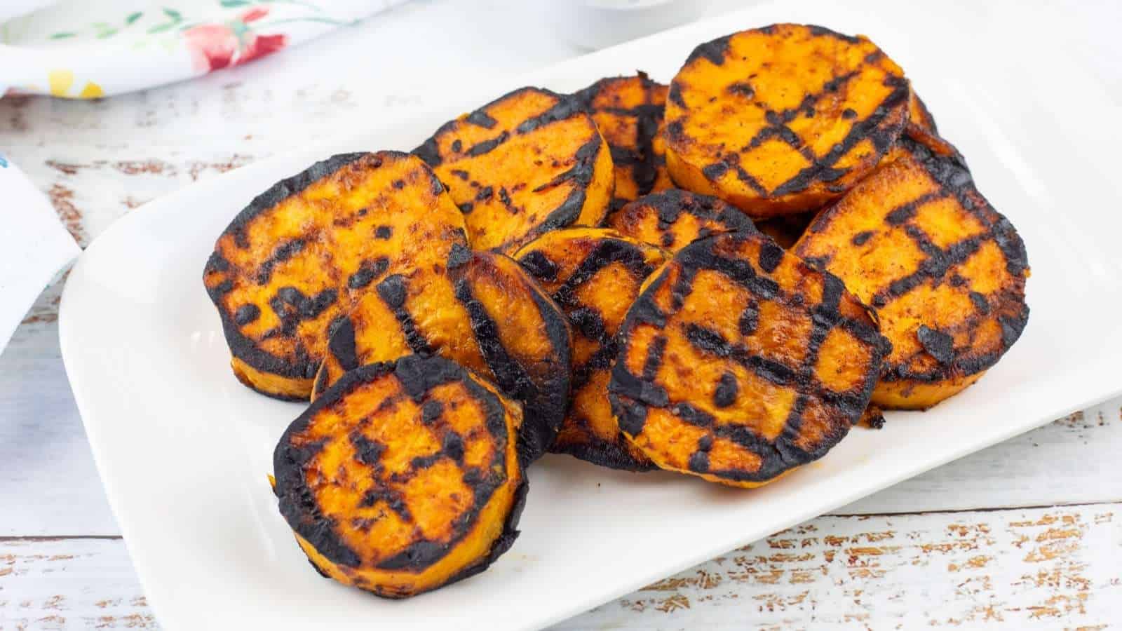 Grilled sweet potato slices with visible char marks arranged on a white rectangular plate.
