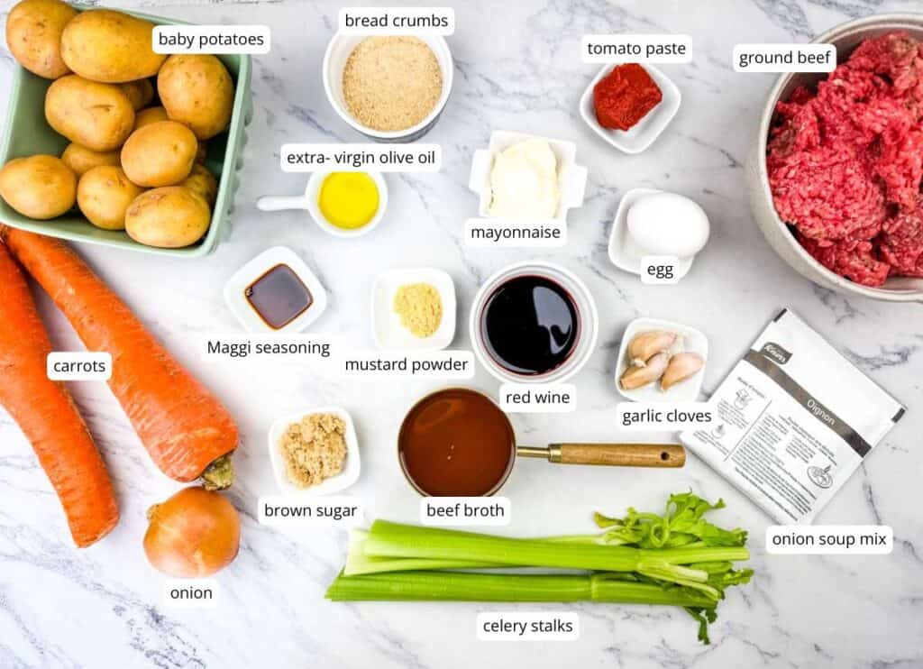 Assorted ingredients for a recipe are arranged on a white surface, including potatoes, carrots, onion, celery, ground beef, and various seasonings, sauces, and condiments.