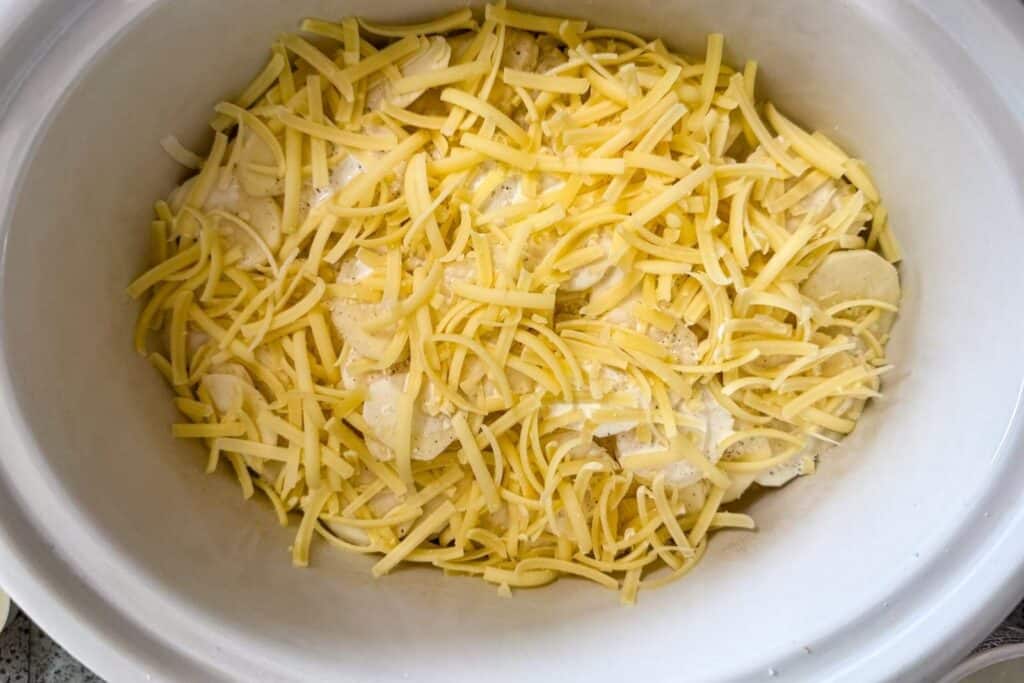 Sliced potatoes topped with shredded cheese in a white baking dish, ready to be cooked.