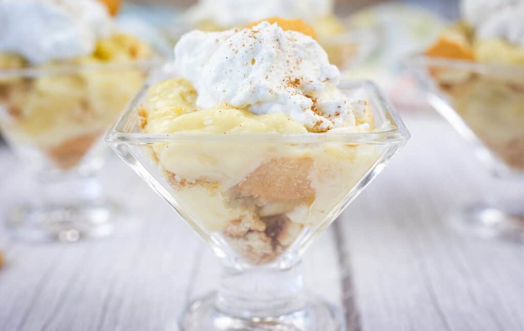 A glass dish filled with banana pudding, layered with vanilla wafers, and topped with whipped cream and a sprinkle of cinnamon.