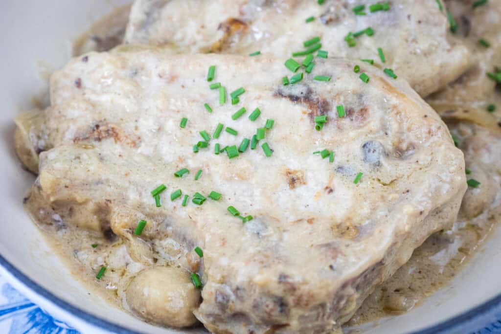 Pork chops covered in a creamy mushroom sauce, garnished with chopped chives.