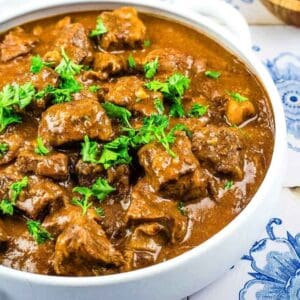 A white bowl filled with beef paprikash garnished with fresh parsley.