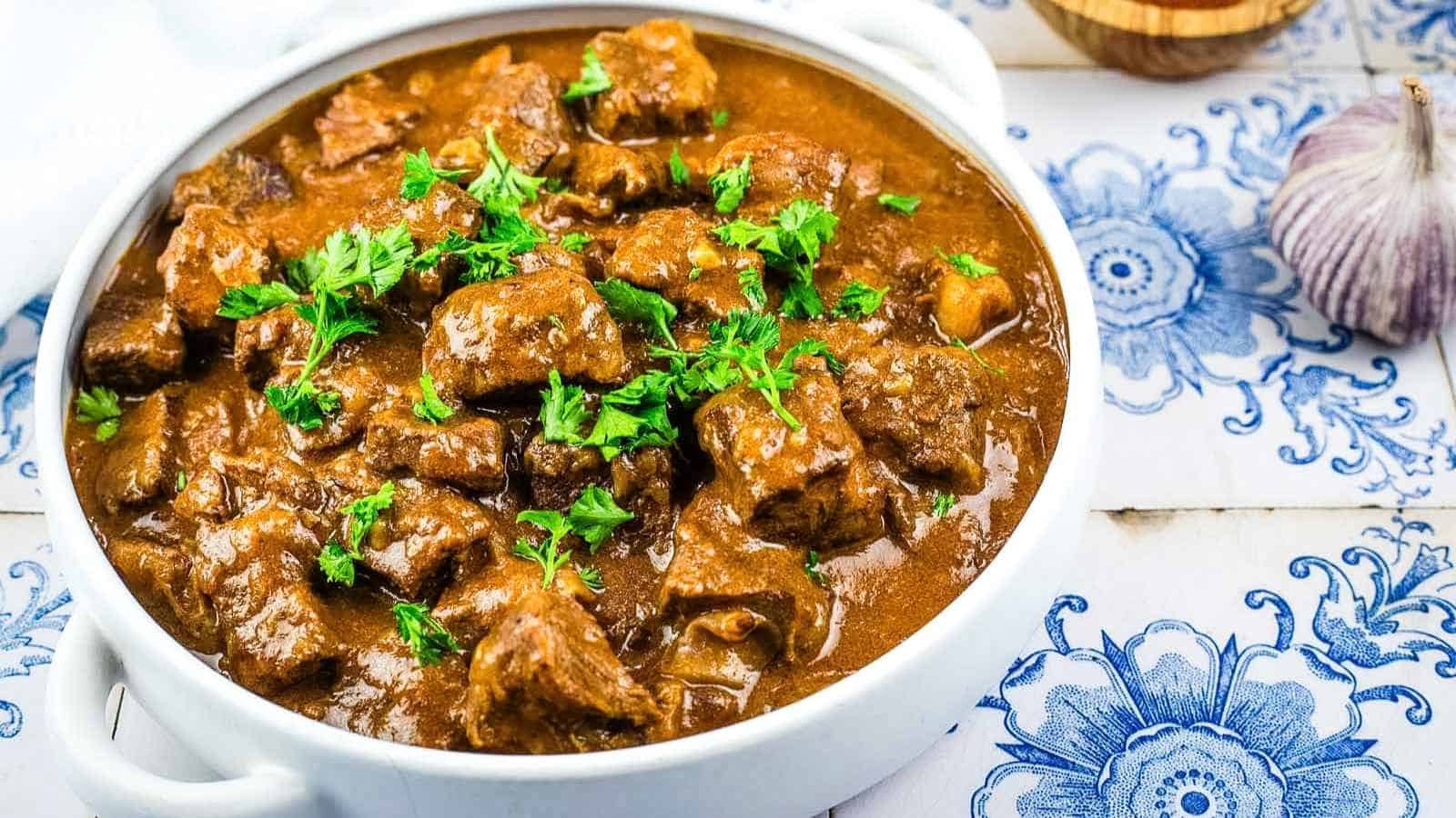 A white bowl filled with beef paprikash garnished with fresh parsley.