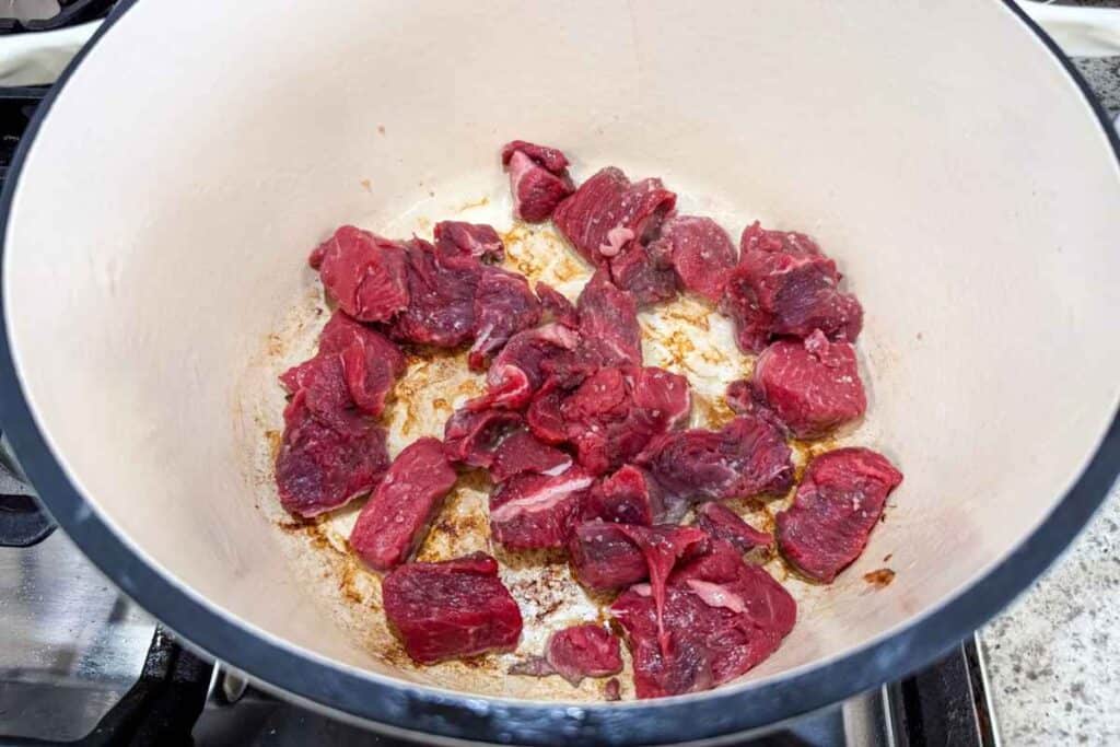 Chunks of raw beef searing in a white enameled cast iron pot.