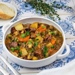 A bowl of beef stew with potatoes, carrots, and mushrooms, served with two slices of bread.