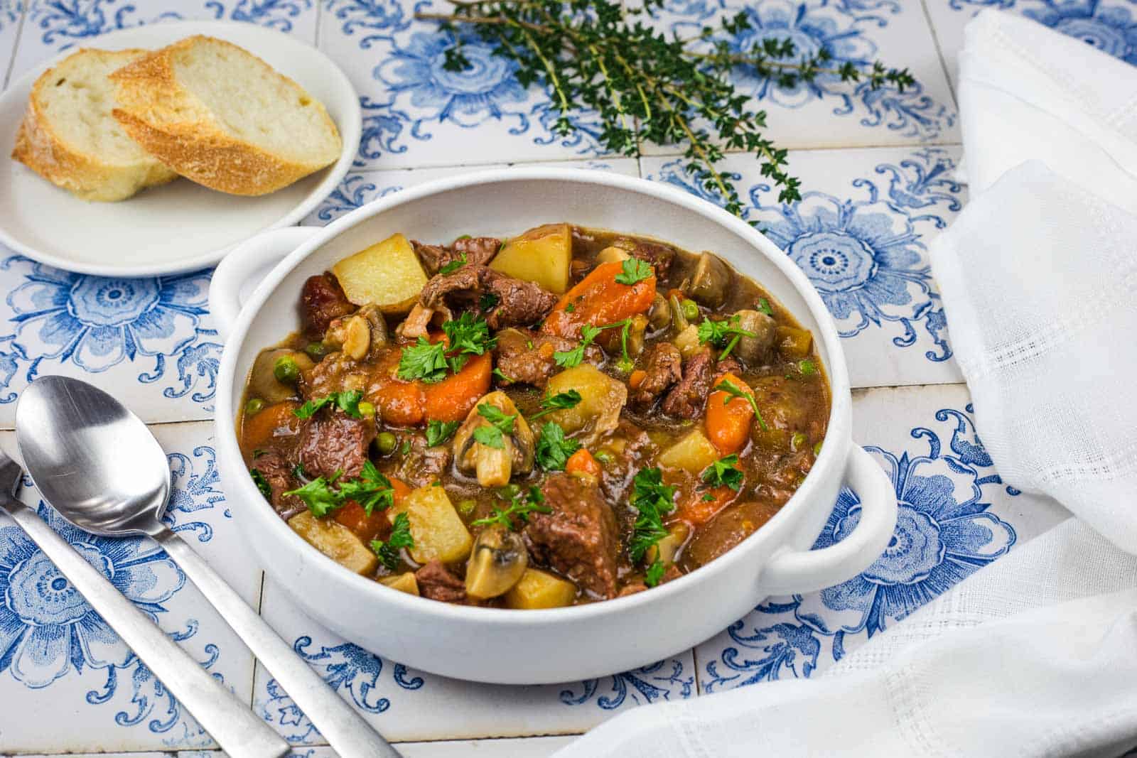 A bowl of beef stew with potatoes, carrots, and mushrooms, served with two slices of bread.